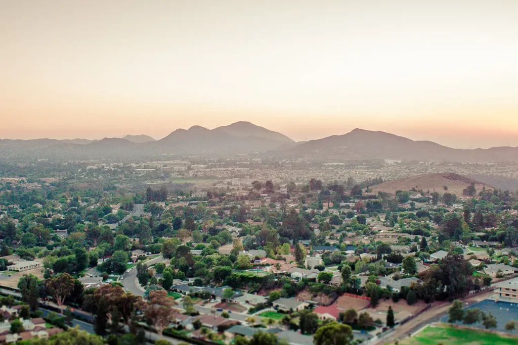 Overlook with single family homes, buildings, and hills in the distance at dusk.