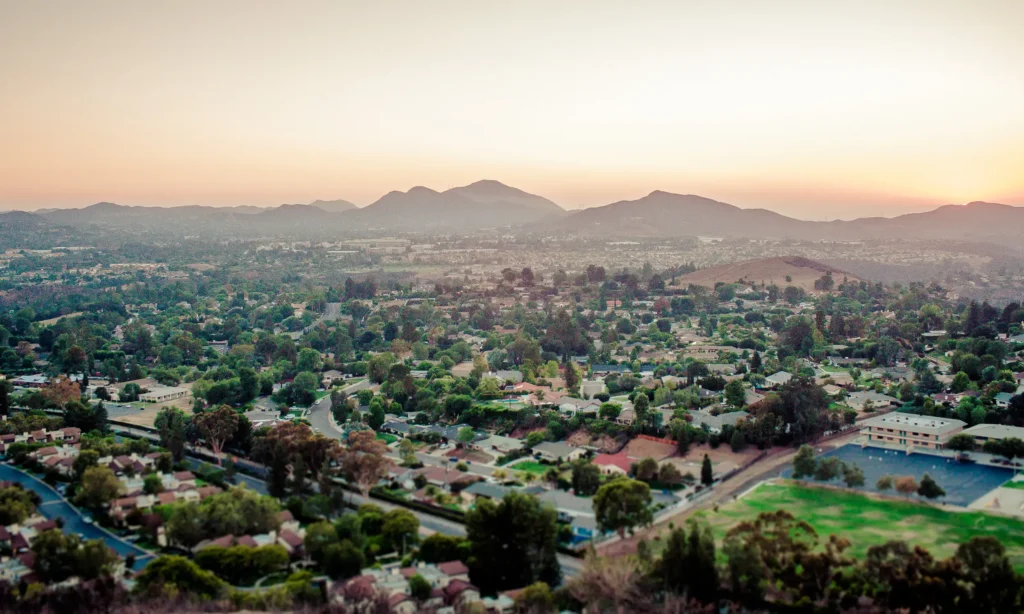 Overlook with single family homes, buildings, and hills in the distance at dusk.