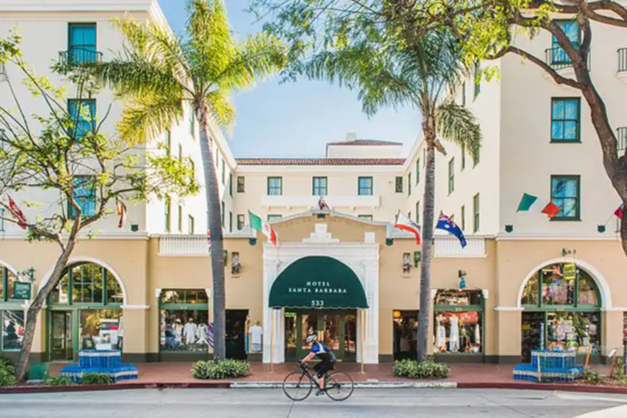 Entrance to Hotel Santa Barbara taken from across the street with a cyclist riding their bike in view.