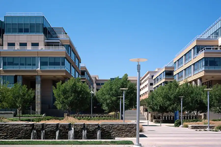 Exterior campus of large office buildings with multiple stories. Paths, lamps, and a staircase are in view.