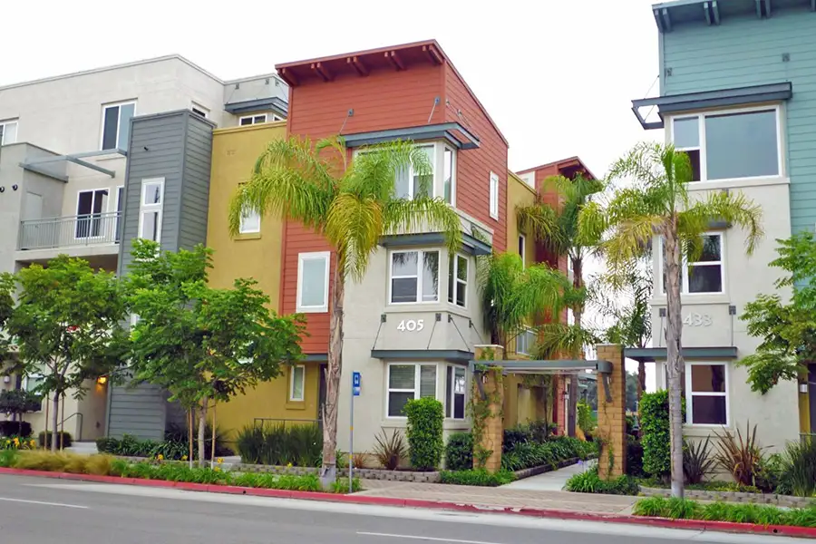 Modern three-story apartment buildings painted in blue and red with palm trees and aditional landscaping.