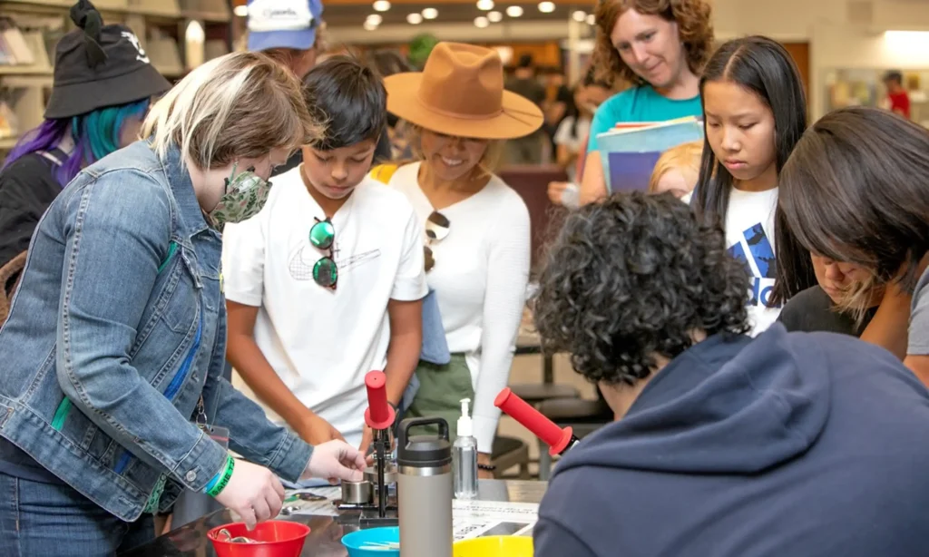 Youth gathered around a microscope examining an object presented by an instructor.