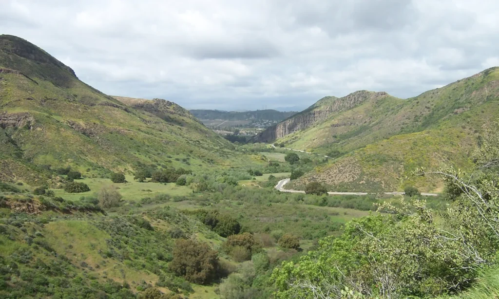 Green rolling hills viewed at the center of a valley with a road winding through the center on an overcast day.