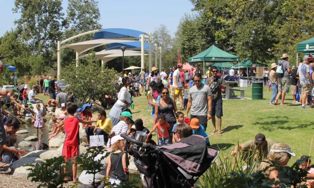 Lots of people at an event at a public park with many children playing in a creek.